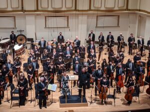 Stacy Garrop, Stéphane Denève, and musicians of the St. Louis Symphony Orchestra standing on stage during applause.