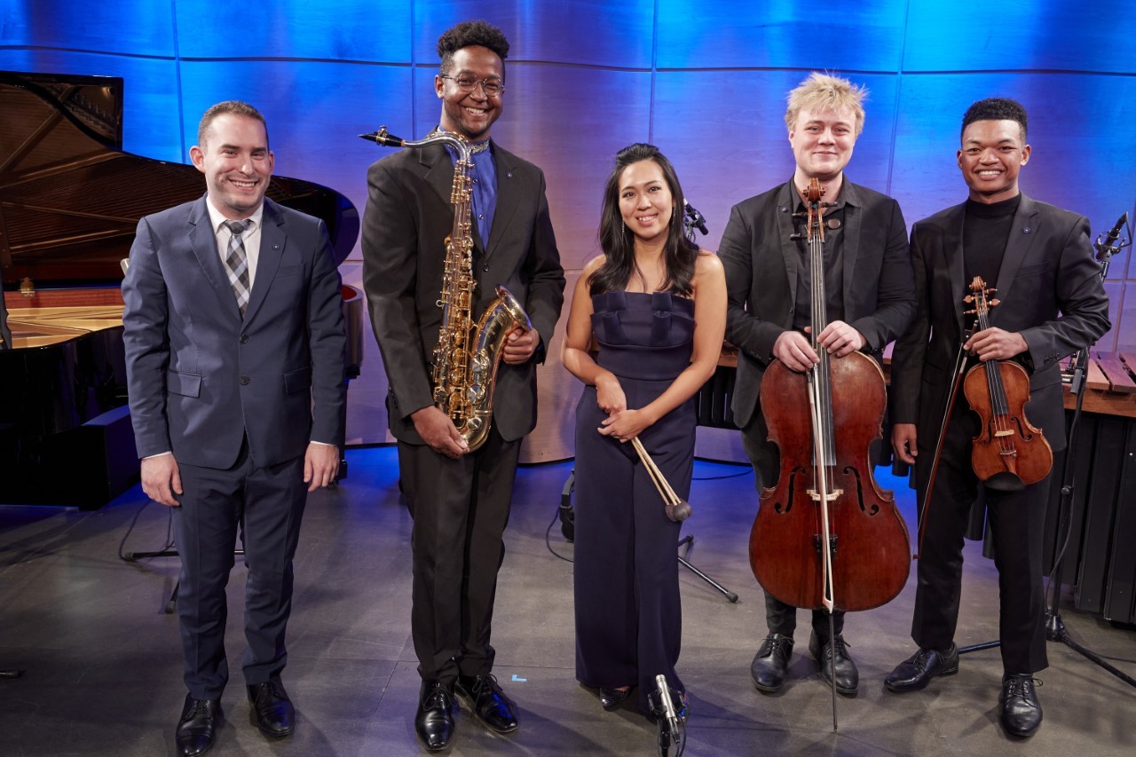 2022 Avery Fisher Career Grant winners standing and posing with their instruments against a blue backdrop.