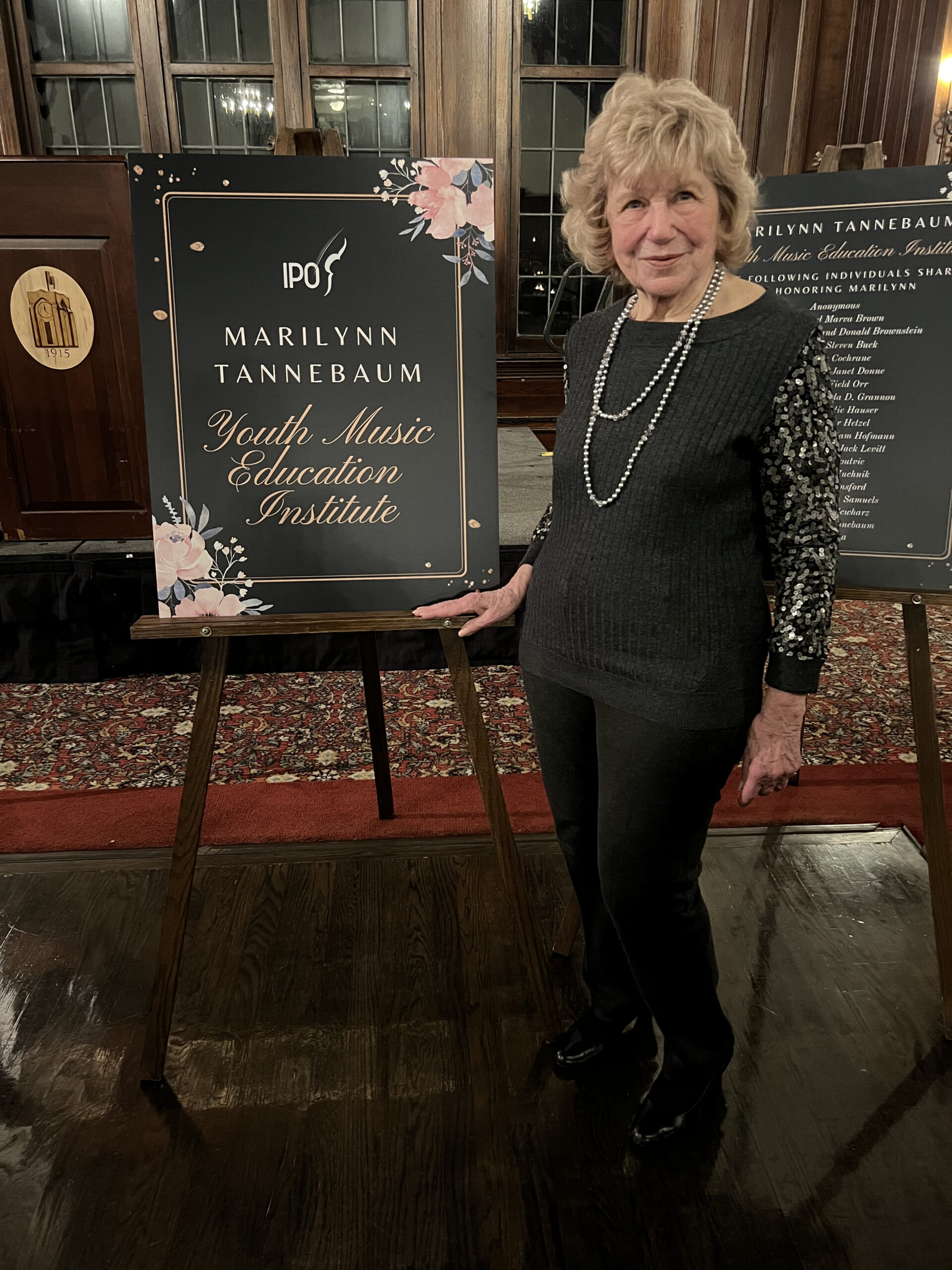Marilyn Tannenbaum posing next to an easel with a sign announcing the new education program named after her.